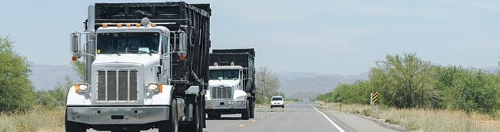 White semi trucks transporting rental construction dumpsters to location on rural road